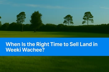A peaceful green field with scattered pine trees under a clear blue sky in Weeki Wachee, Florida. A bold blue banner across the bottom reads “When Is the Right Time to Sell Land in Weeki Wachee?”